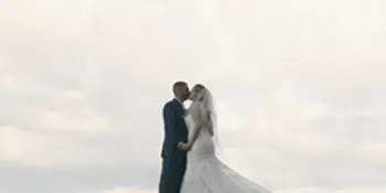 Bride and groom embracing on a grassy hill under an overcast sky