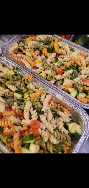 Large aluminum catering trays filled with tri-color rotini pasta salad mixed with vegetables.