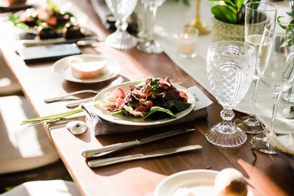 A plated salad dish served on a wooden table with crystal glassware and silverware.