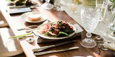 A plated salad dish served on a wooden table with crystal glassware and silverware.