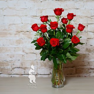 A bouquet of red roses in a clear glass vase against a white brick wall.
