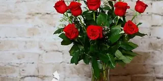 A bouquet of red roses in a clear glass vase against a white brick wall.