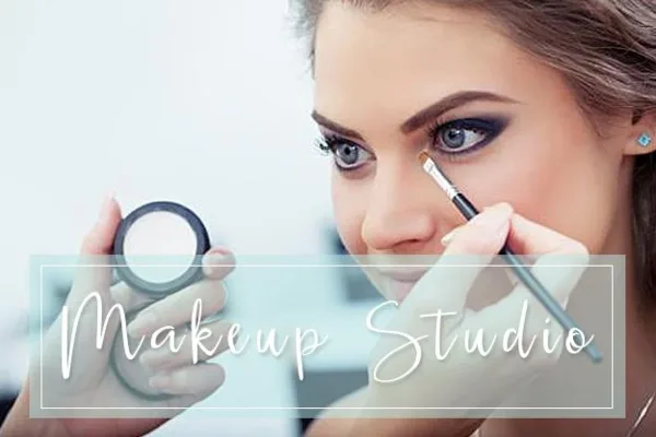 A makeup artist applying eye makeup to a client using a brush and a compact mirror.