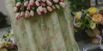 A close-up of a handcrafted floral basket made of pink tulips and green leaves, held by a person wearing a floral dress.