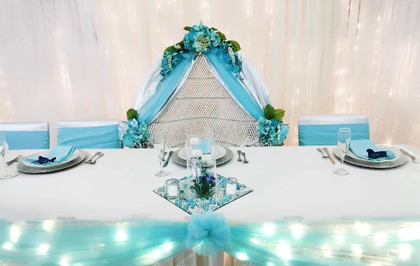 A decorated event table with a blue floral arch, white tablecloth, and place settings.