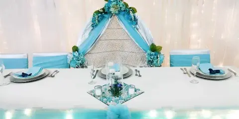 A decorated event table with a blue floral arch, white tablecloth, and place settings.