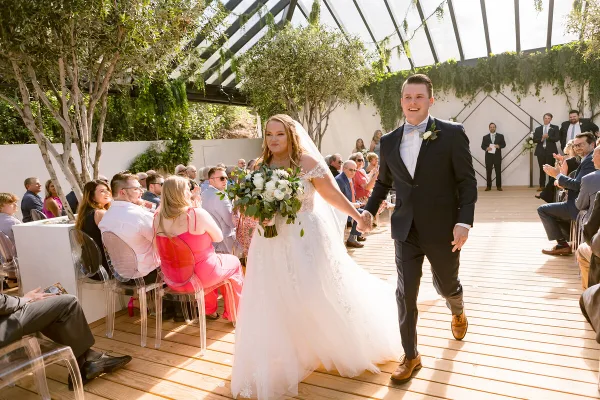 A bride and groom walking down the aisle during a wedding ceremony in a glass-walled venue.