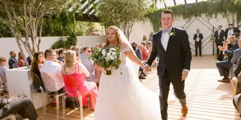 A bride and groom walking down the aisle during a wedding ceremony in a glass-walled venue.