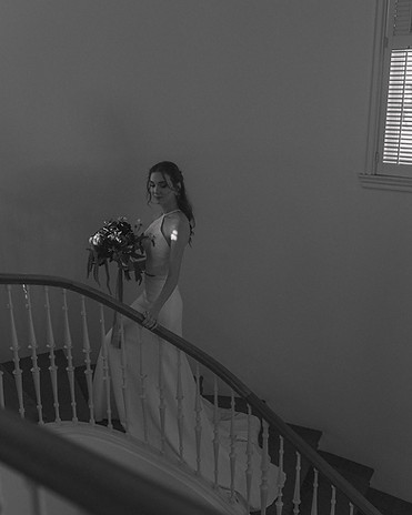 A bride in a white gown holding a bouquet while standing on a curved staircase.