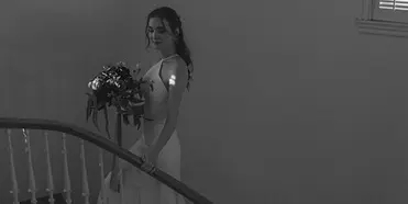A bride in a white gown holding a bouquet while standing on a curved staircase.