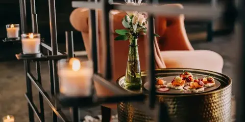 A plated appetizer garnished with fresh herbs and a small floral arrangement in a glass vase, set on a metallic table.