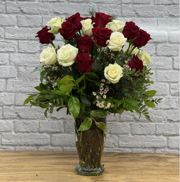 A floral arrangement featuring red and white roses and greenery in a clear glass vase.