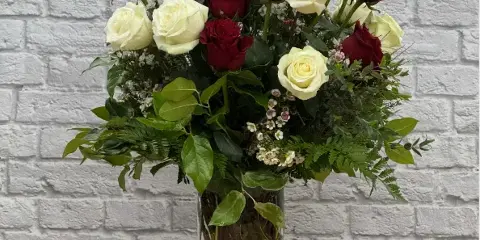 A floral arrangement featuring red and white roses and greenery in a clear glass vase.