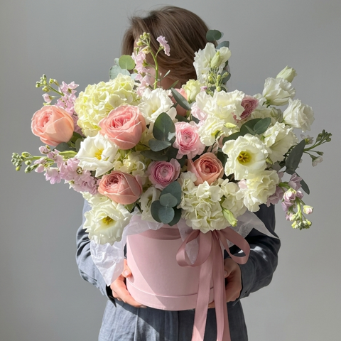 A person holding a large bouquet of pink and white flowers in a pink container.