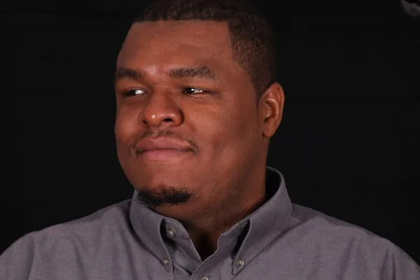 Portrait of a man in a grey button-down shirt against a dark background
