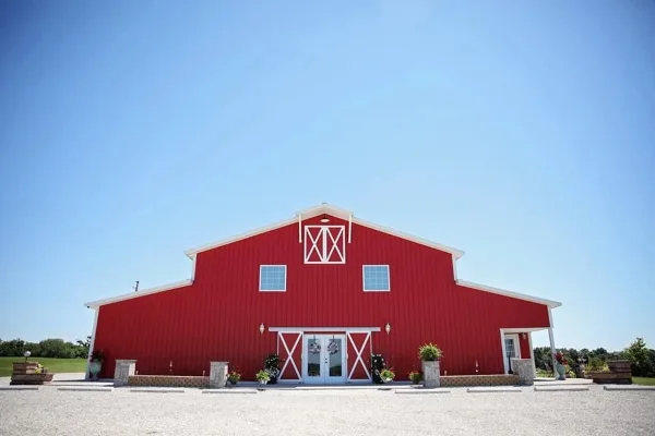 Exterior view of a large red barn-style wedding venue with white trim and a gravel driveway.