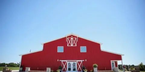 Exterior view of a large red barn-style wedding venue with white trim and a gravel driveway.