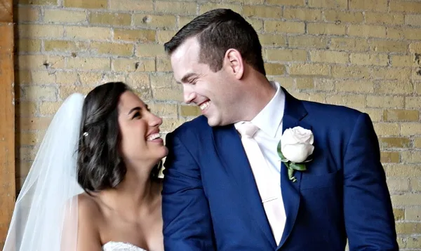 A bride and groom smiling at each other in front of a brick wall