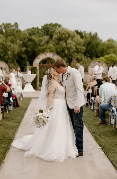 A bride and groom kiss at the end of the aisle during an outdoor wedding ceremony.