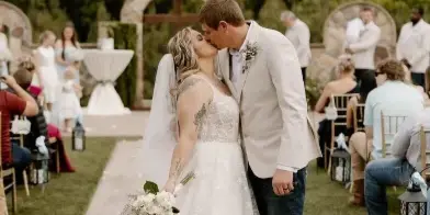 A bride and groom kiss at the end of the aisle during an outdoor wedding ceremony.