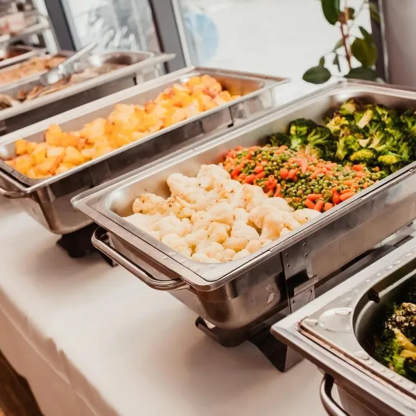 A catering buffet line featuring stainless steel chafing dishes filled with prepared cauliflower, potatoes, and mixed vegetables.