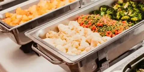 A catering buffet line featuring stainless steel chafing dishes filled with prepared cauliflower, potatoes, and mixed vegetables.