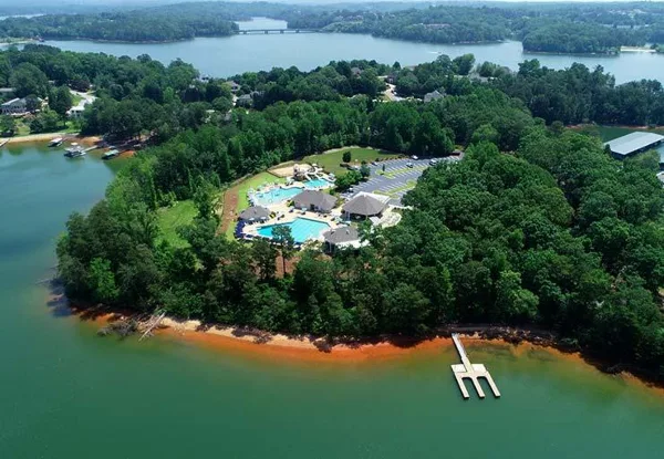 Aerial view of a private country club with a pool, pavilions, and marina situated on a wooded peninsula on a lake.