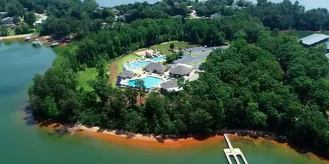 Aerial view of a private country club with a pool, pavilions, and marina situated on a wooded peninsula on a lake.