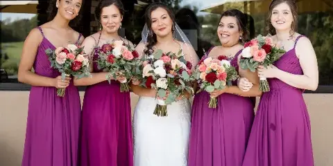 A bride and four bridesmaids in purple dresses holding colorful wedding bouquets.