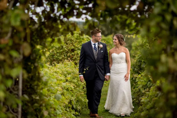 A bride and groom walking hand-in-hand through a lush green vineyard.