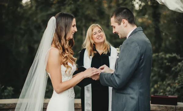 A wedding officiant standing between a bride and groom during a ceremony as they exchange rings.