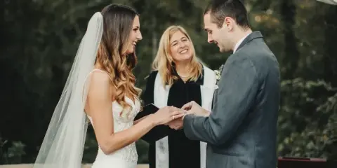 A wedding officiant standing between a bride and groom during a ceremony as they exchange rings.