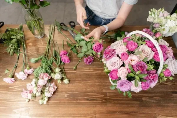 A florist arranging a bouquet of pink and white flowers on a wooden table.