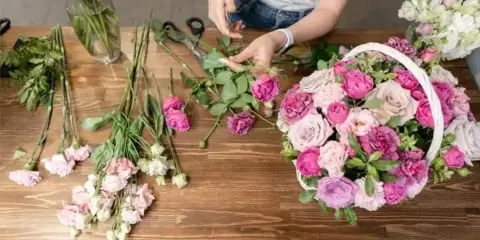 A florist arranging a bouquet of pink and white flowers on a wooden table.