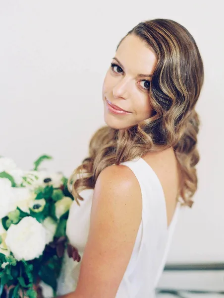A bride with styled wavy hair and makeup holding a white floral bouquet.