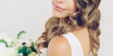 A bride with styled wavy hair and makeup holding a white floral bouquet.