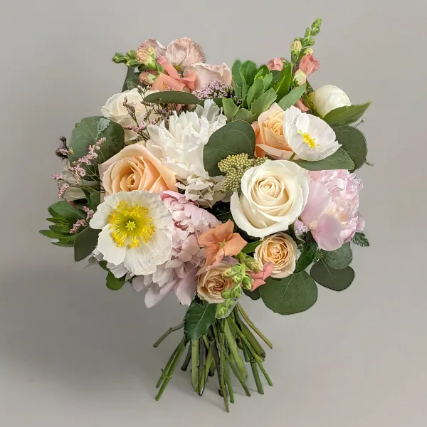 A hand-tied floral bouquet containing white and peach roses, ranunculus, and greenery against a neutral background.