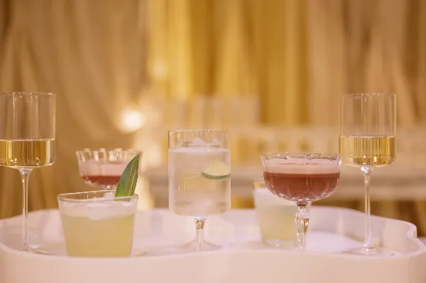 A tray of assorted cocktails and champagne glasses set against a warm, draped background.