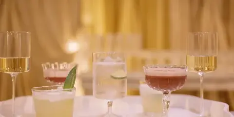 A tray of assorted cocktails and champagne glasses set against a warm, draped background.