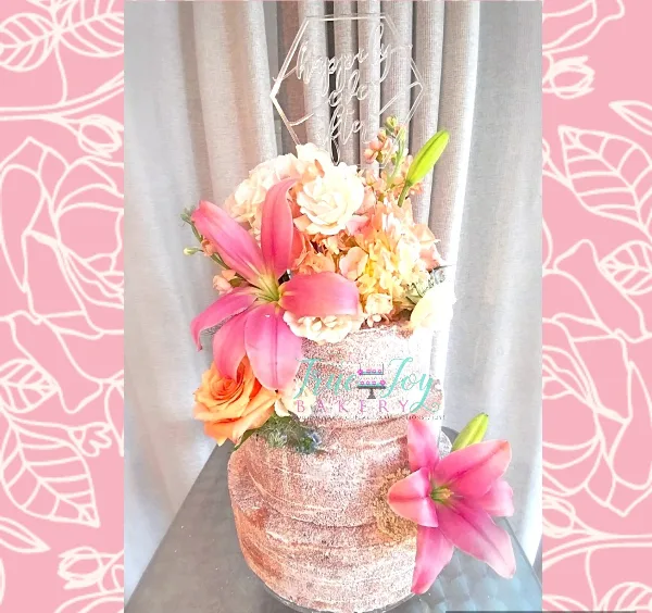 A custom wedding cake decorated with pink lilies and roses, topped with a 'Happily Ever After' acrylic sign.