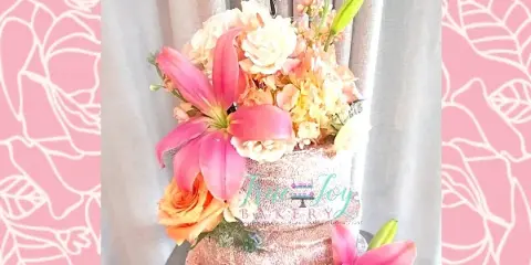 A custom wedding cake decorated with pink lilies and roses, topped with a 'Happily Ever After' acrylic sign.