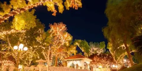 Nighttime view of an outdoor wedding venue featuring a gazebo, white chairs, and trees illuminated with string lights.