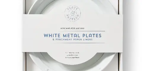 A set of white metal plates and parchment paper liners in a white box.
