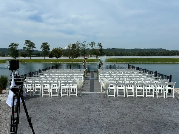 Outdoor wedding ceremony setup with white chairs and a floral arch overlooking a river.
