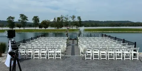 Outdoor wedding ceremony setup with white chairs and a floral arch overlooking a river.