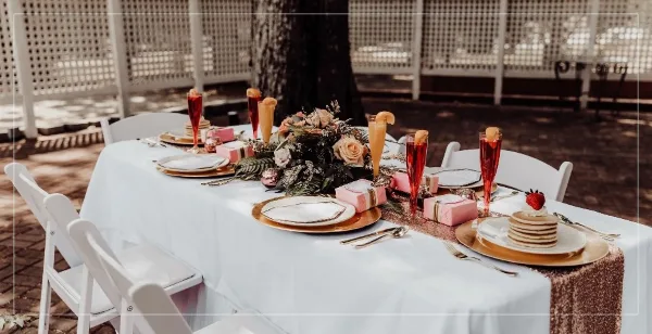 A wedding reception table set with white linens, floral arrangements, and champagne flutes at an outdoor venue.