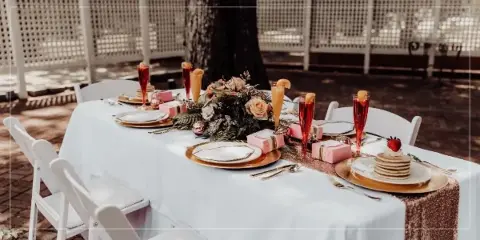 A wedding reception table set with white linens, floral arrangements, and champagne flutes at an outdoor venue.