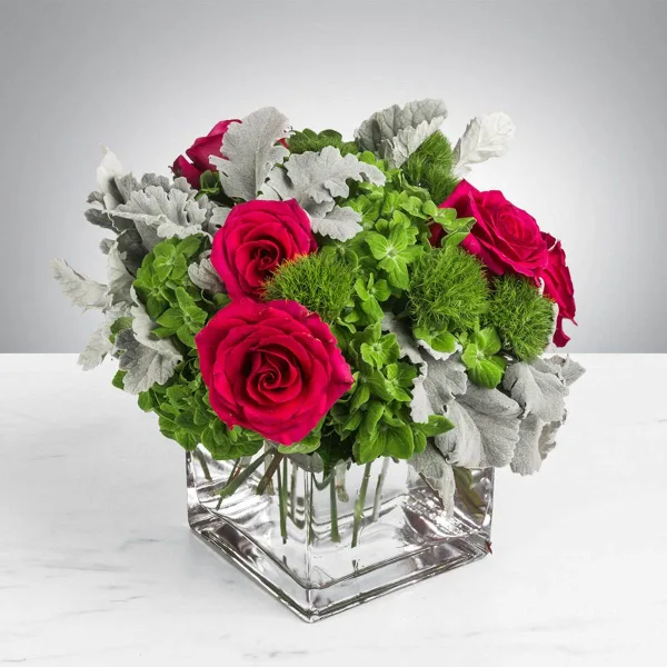 A floral arrangement with pink roses, green hydrangeas, and dusty miller in a clear glass vase.
