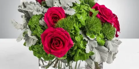 A floral arrangement with pink roses, green hydrangeas, and dusty miller in a clear glass vase.