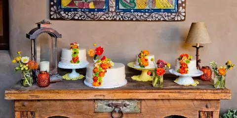 A rustic wooden table displays multiple white wedding cakes decorated with colorful flowers, arranged with candles and floral accents.
